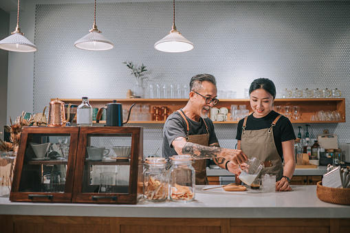 Barista chino senior asiático enseñando a su hija a hacer café en el mostrador del café bar photo