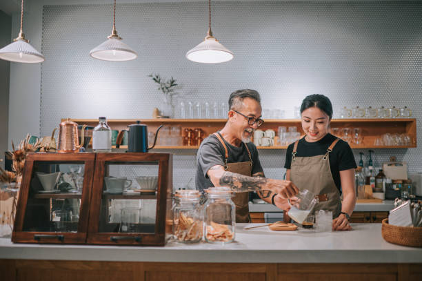 barista masculin chinois âgé asiatique enseignant à sa fille de faire du café au comptoir du café-bar - établissement de restauration photos et images de collection