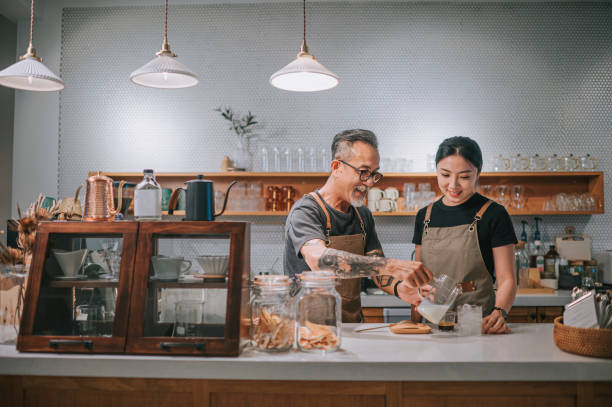 asian chinese senior male barista teaching his daughter making coffee at cafe bar counter - family business stockfoto's en -beelden