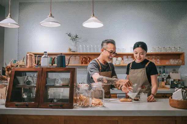 Photo of asian chinese senior male barista teaching his daughter making coffee at cafe bar counter