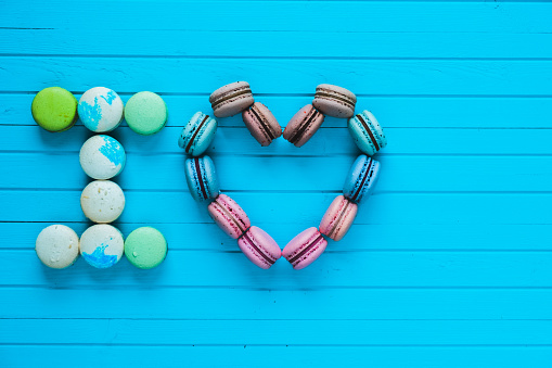 I love - multicolored macaroons in the form of hearts and confessions of lovers lie on a turquoise wooden background, copy space.