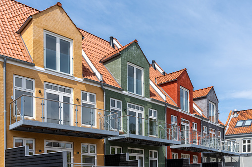Svendborg, Denmark - 10 June, 2021: modern colorful wooden row houses with balconies and separated patios under a blue sky with wispy clouds