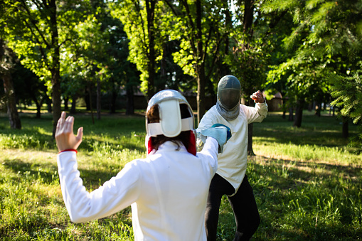 Two young adults are practicing fencing outdoors on a sunny day