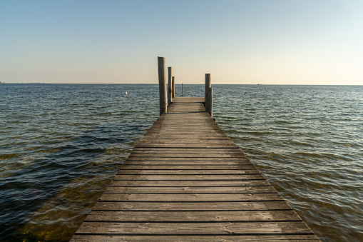 A wooden dock leading out into a calm blue ocean in evening light