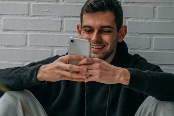 istock young man looking at mobile phone sitting at home smiling 1326505399