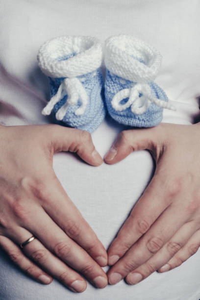 Mom's hands in the shape of heart with booties on the stomach closeup, upright Mom's hands in the shape of heart with booties on the stomach close-up, upright good posture photos stock pictures, royalty-free photos & images
