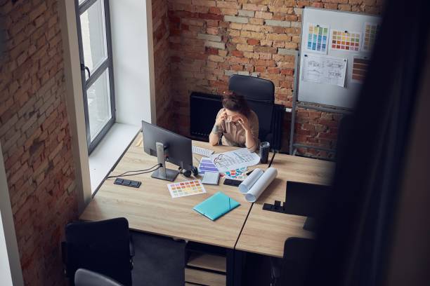 istock High angle view of tired woman touching her temples, having a stong headache while working on new project, using pc in modern office 1326510838