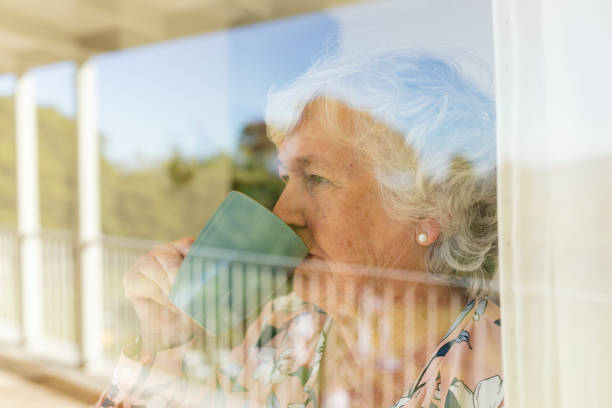 istock Senior caucasian woman looking through window holding mug and drinking 1326511458