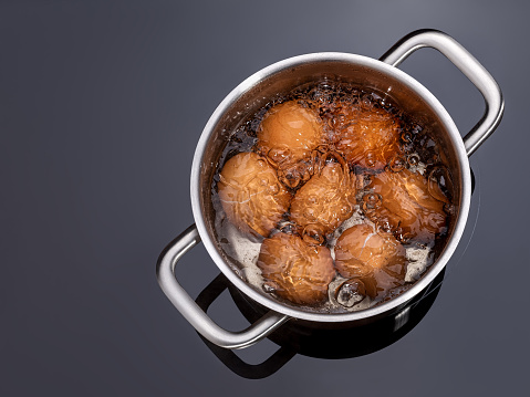 Chicken eggs are boiled in a saucepan on a glass ceramic induction hob. Cooking hard boiled eggs in a metal pan on electric stove. Brown shell eggs in a pot of hot water with bubbles. Top view.