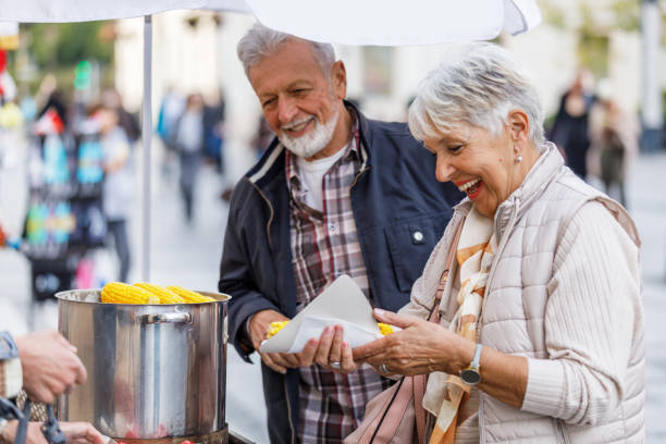 portret starszego mężczyzny i jego żony w city walk eating corn. - dining senior adult friendship mature adult zdjęcia i obrazy z banku zdjęć