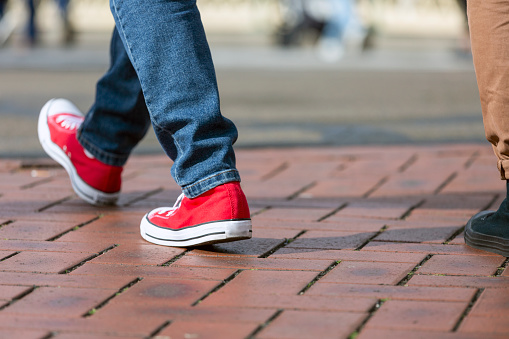 Closeup legs of young man walking in city in red sneakers, background with copy space, full frame horizontal composition