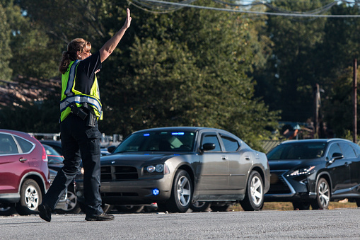 Suwanee, GA, USA - September 21, 2019:  A female police officer puts her hand up to stop traffic, as she directs vehicle traffic at an intersection at a local fall festival on September 21, 2019 in Suwanee, GA.