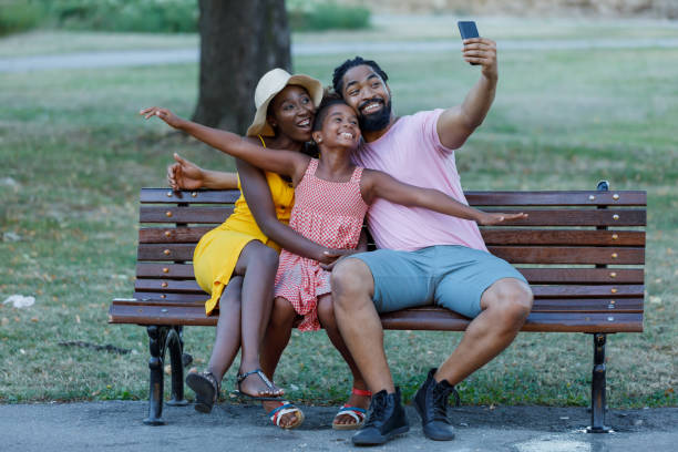 junge afroamerikanische familie macht selfie-foto in public park und spielt mit einer niedlichen kleinen tochter. - holding men casual mother stock-fotos und bilder