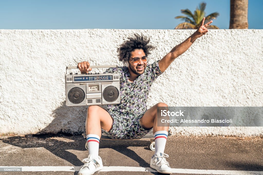 Young Afro Latin man having fun listening music with headphones and vintage boombox during summer vacations Boom Box Stock Photo