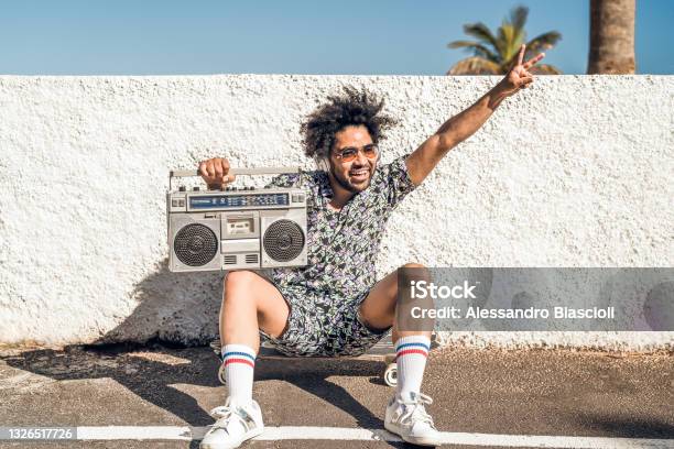 Young Afro Latin Man Having Fun Listening Music With Headphones And Vintage Boombox During Summer Vacations Stock Photo - Download Image Now