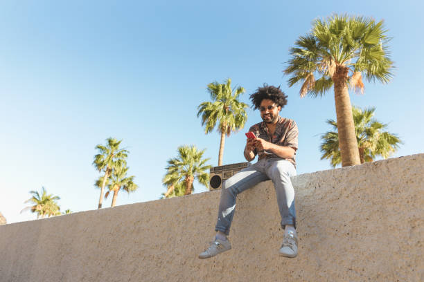 istock Happy Afro man having fun using mobile smartphone while listening to music with vintage boombox stereo in tropical place during summer vacations 1326517767