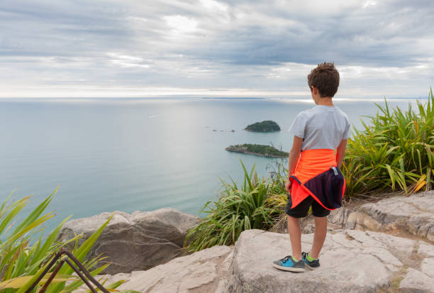 Young boy with orange vest around waste standing on rock in mountain looking at view across ocean. Mount Maunganui New Zealand -January 21 2015; Young boy with orange vest around waste standing on rock in mountain looking at view across ocean. mount maunganui stock pictures, royalty-free photos & images