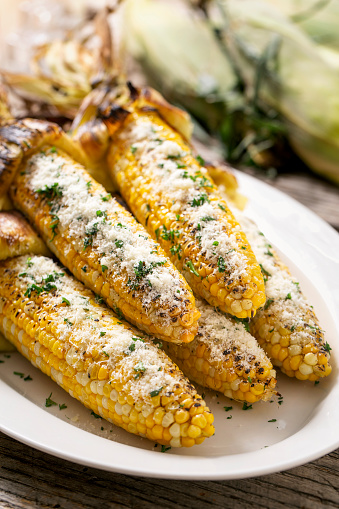 Grilled Mexican corn on the cob with parmesan cheese on rustic wood table and charred husk.