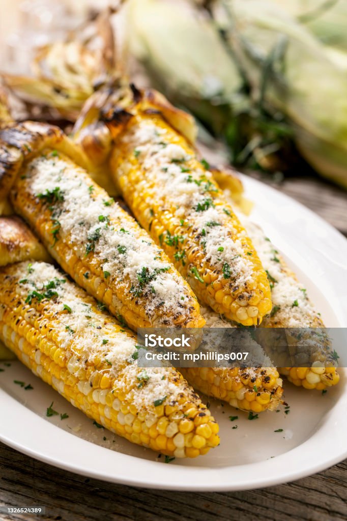 Grilled Corn on The Cob With Parmesan Cheese Grilled Mexican corn on the cob with parmesan cheese on rustic wood table and charred husk. Corn Stock Photo
