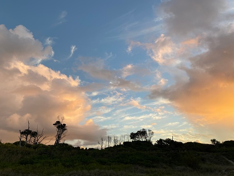 Horizontal landscape photo of a dramatic sunset sky above scrub forest and sand dunes in silhouette in the foreground as seen from the beach at Byron Bay, north coast of NSW