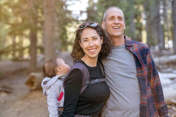 Happy multi-generation family enjoying nature hike A young mixed race woman carries her one year old daughter on her back in an ergonomic baby carrier while out on a hike. The woman is enjoying time with her father. The multi-generation family family is staying active and healthy outdoors in Oregon. legacy concept photos stock pictures, royalty-free photos & images