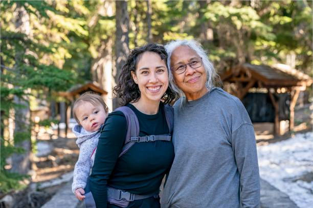 Happy multi-generation family enjoying nature hike A young mixed race woman carries her one year old daughter on her back in an ergonomic baby carrier while out on a hike with her senior mother. The multi-generation family is staying active and healthy outdoors in Oregon. legacy concept photos stock pictures, royalty-free photos & images