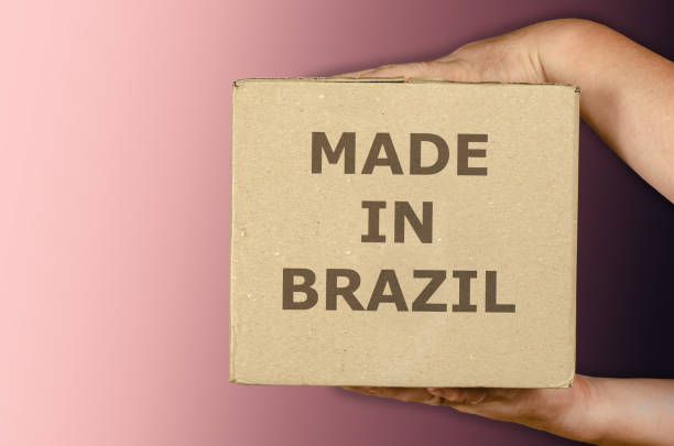 istock Hands holding cardboard box of Brazilian merchandise on colored gradient background. 1326530784