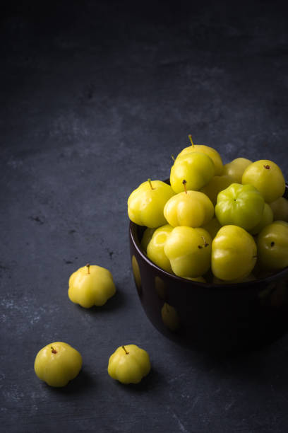 star gooseberry or starberry, also known as malay or country or west india or tahitian gooseberry, small star shaped waxy yellow tropical berries fruit in a cup, darker textured background