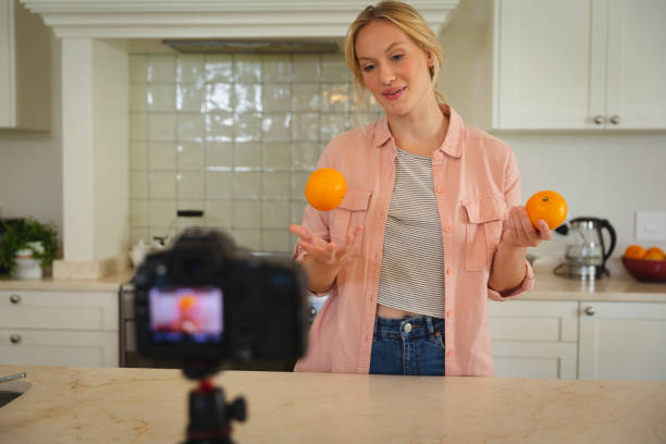 istock Smiling caucasian woman in kitchen holding oranges and using camera, making cooking vlog 1326550855