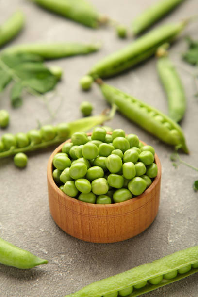 istock Green peas in wooden bowl on grey background 1326558053