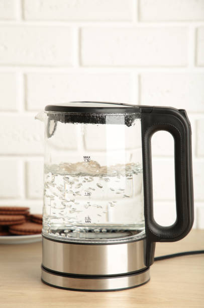 istock Glass electric kettle with boiling water and chocolate chip cookie on white background. 1326558821