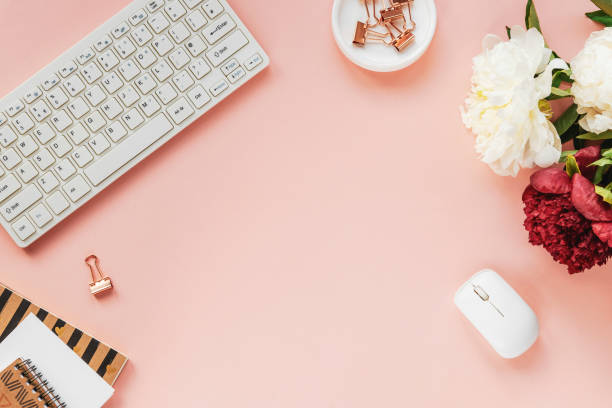 istock Woman workplace with peony flowers, notepad, computer keyboard and computer mouse. Top view, flat lay. Pink background 1326561020