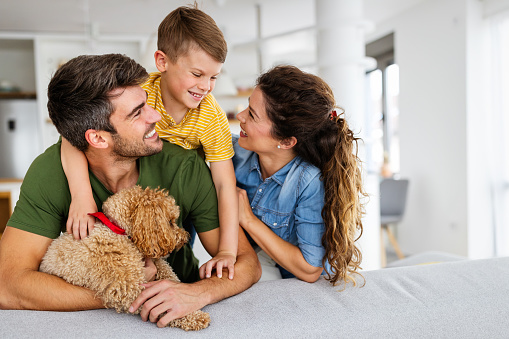 Full length shot of young boy and his father sitting on the living room floor and cuddling their yellow Labrador Retriever.