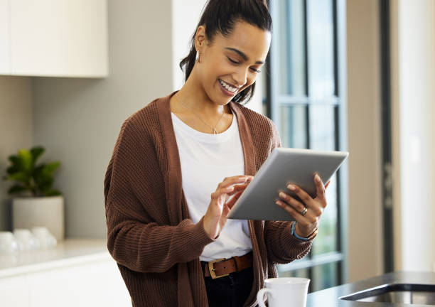 Shot of a young woman using a digital tablet at home Let's see if my favourite store has any new arrivals using digital tablet stock pictures, royalty-free photos & images
