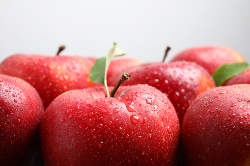 Delicious ripe red apples with water drops on light grey background, closeup