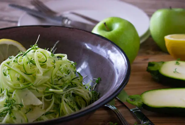 fresh and raw salad with green apples and zucchini marinated with fresh lemon juice and served in a rustic enamel bowl on kitchen table. Front view
