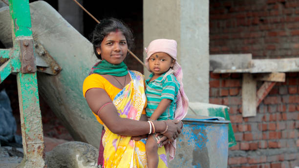Jamshedpur, Jharkhand, India - June 1 2020: Young Indian woman working at construction site with her baby in her lap at Jamshedpur