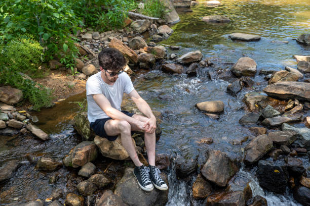 istock Sad young man sits alone on a stone in a flowing stream 1326575281
