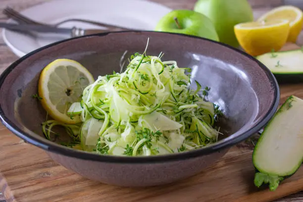 fresh zucchini salad with green apples marinated with lemon juice and olive oil and served in a rustic enamel bowl on kitchen table background