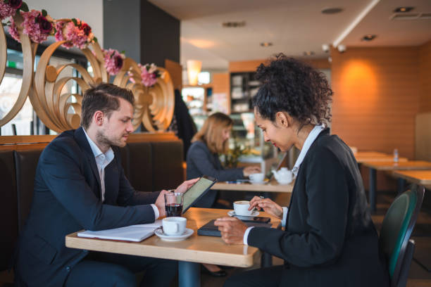 Caucasian businessman and a Latin businesswoman collaborating on a business project sitting comfortably in a cafeteria using a digital tablet.