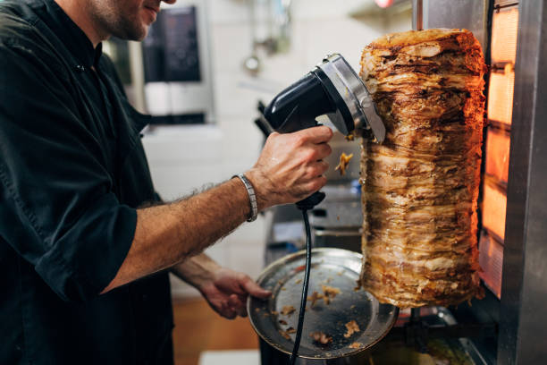 Focused professional chef, in the kitchen, using the electric tool/rotated knife to cut the kebab/gyros, while meat spinning and grilling on the gyros grill