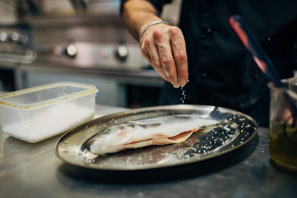 chef condire la spigola con un pizzico di sale - prepared fish foto e immagini stock