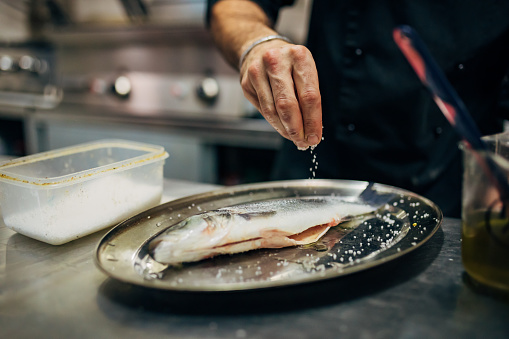In the modern kitchen, a professional male chef, season the sea bass with salt, to gain an extra taste of the fish