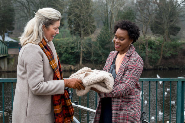 Sustainable Homemade Fashion Medium shot of a woman selling a handmade ethically sourced woollen cardigan. She is showing the garment to a woman who has met her in the park to purchase it. clothing swap photos stock pictures, royalty-free photos & images