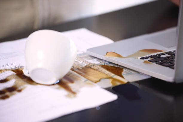 nahaufnahme von kaffee über einem laptop verschüttet und papierkram auf einem tisch - spilling stock-fotos und bilder