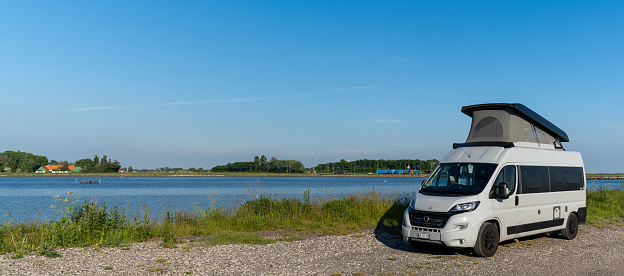 Tars, Denmark - 10 June, 2021- gray camper van parked on a gravel road at the ocean shore of Lolland Island in southern Denmark