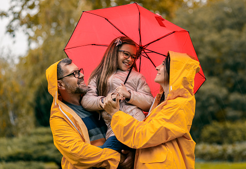 Family of three in raincoat enjoying together in city park.