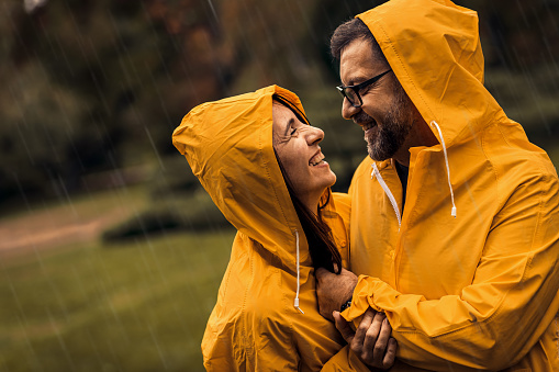 Portrait of mid adult couple in raincoat enjoying together on rain in city park.