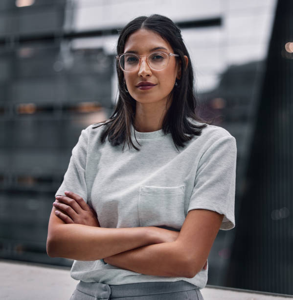 foto de una atractiva joven empresaria sola en la oficina con los brazos cruzados durante un turno tardío - beauty beautiful brown hair black hair fotografías e imágenes de stock