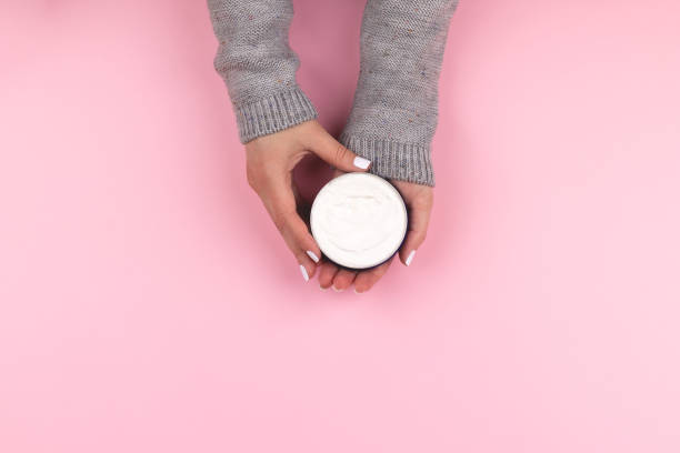 Hands holding jar with cream on pink background